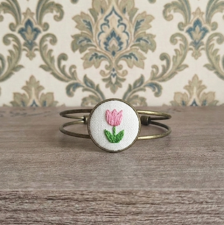 Bracciale artigianale Fildisogno con simbolo ricamato in tessuto colorato e dettagli dettagliati.