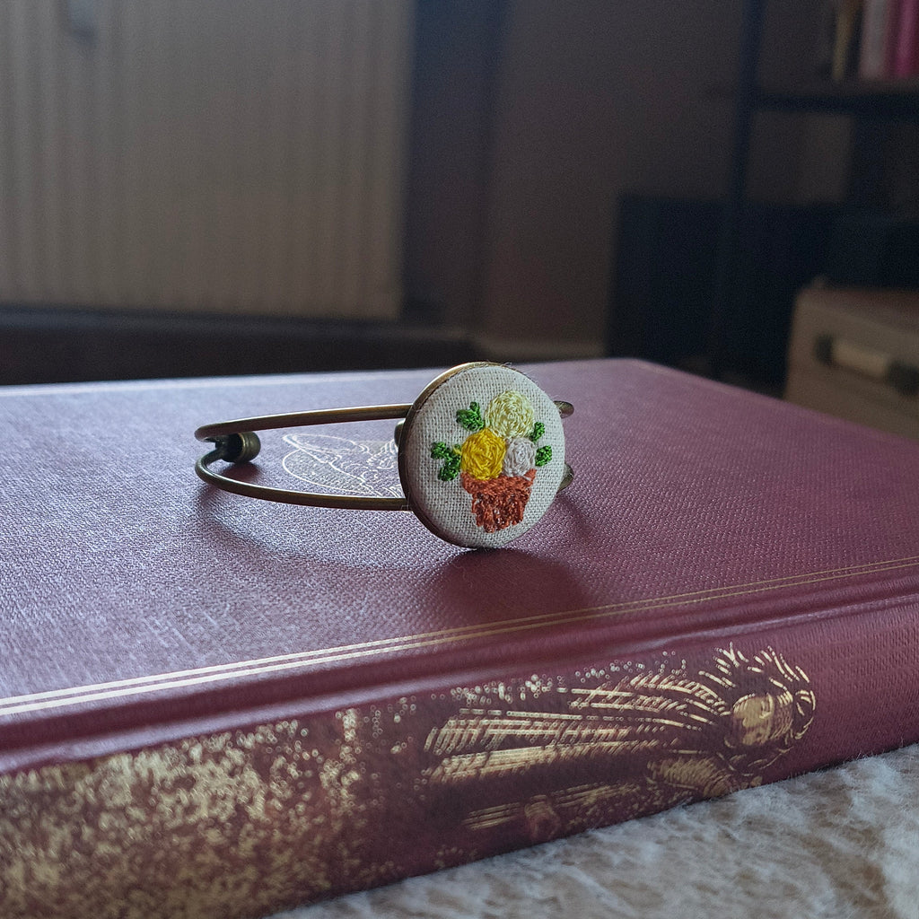 Bracciale artigianale Fildisogno con simbolo ricamato, dettaglio ricco e decorativo, in tessuto colorato.