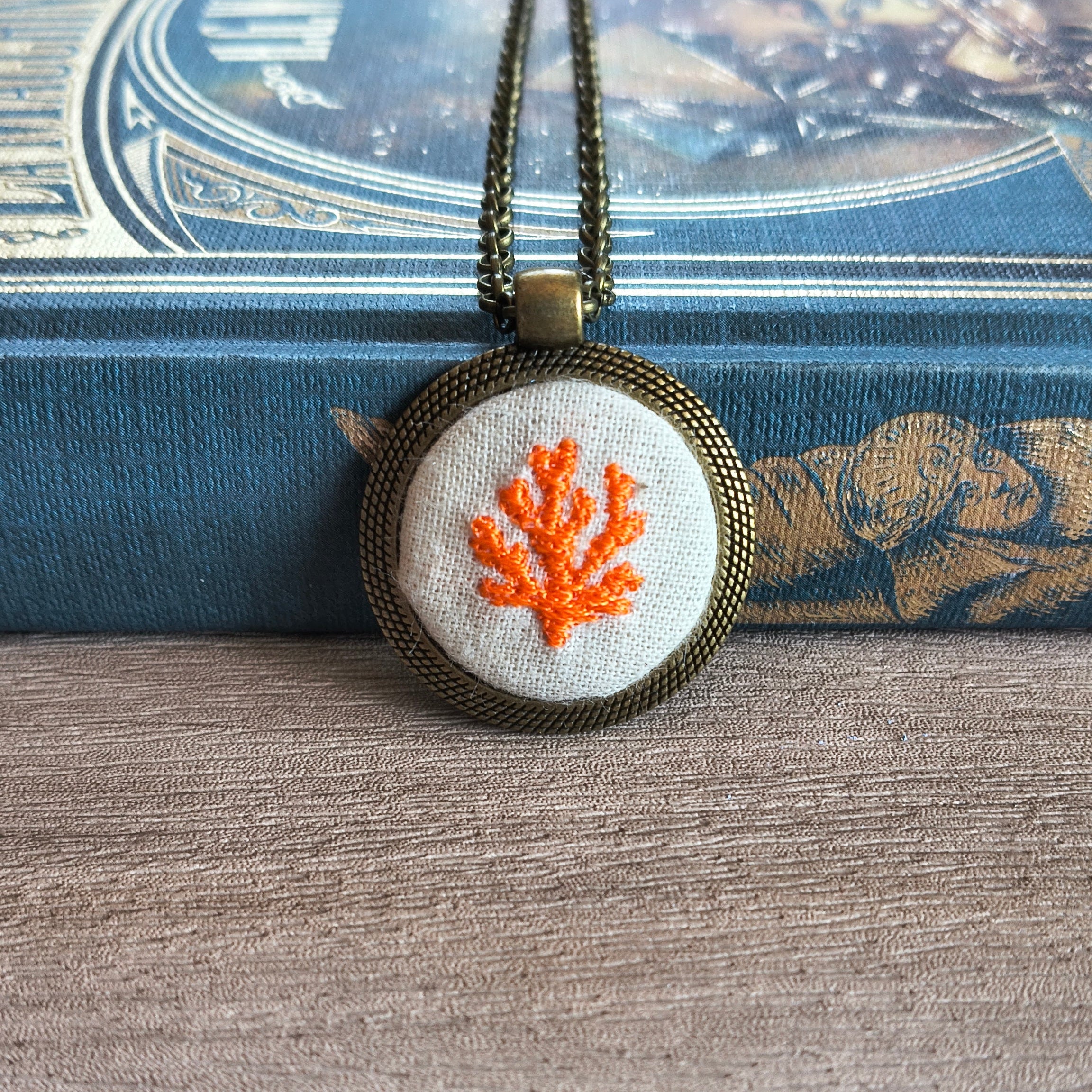 Collana con simbolo ricamato artigianale di Fildisogno, dettaglio di un ricamo colorato su tessuto.