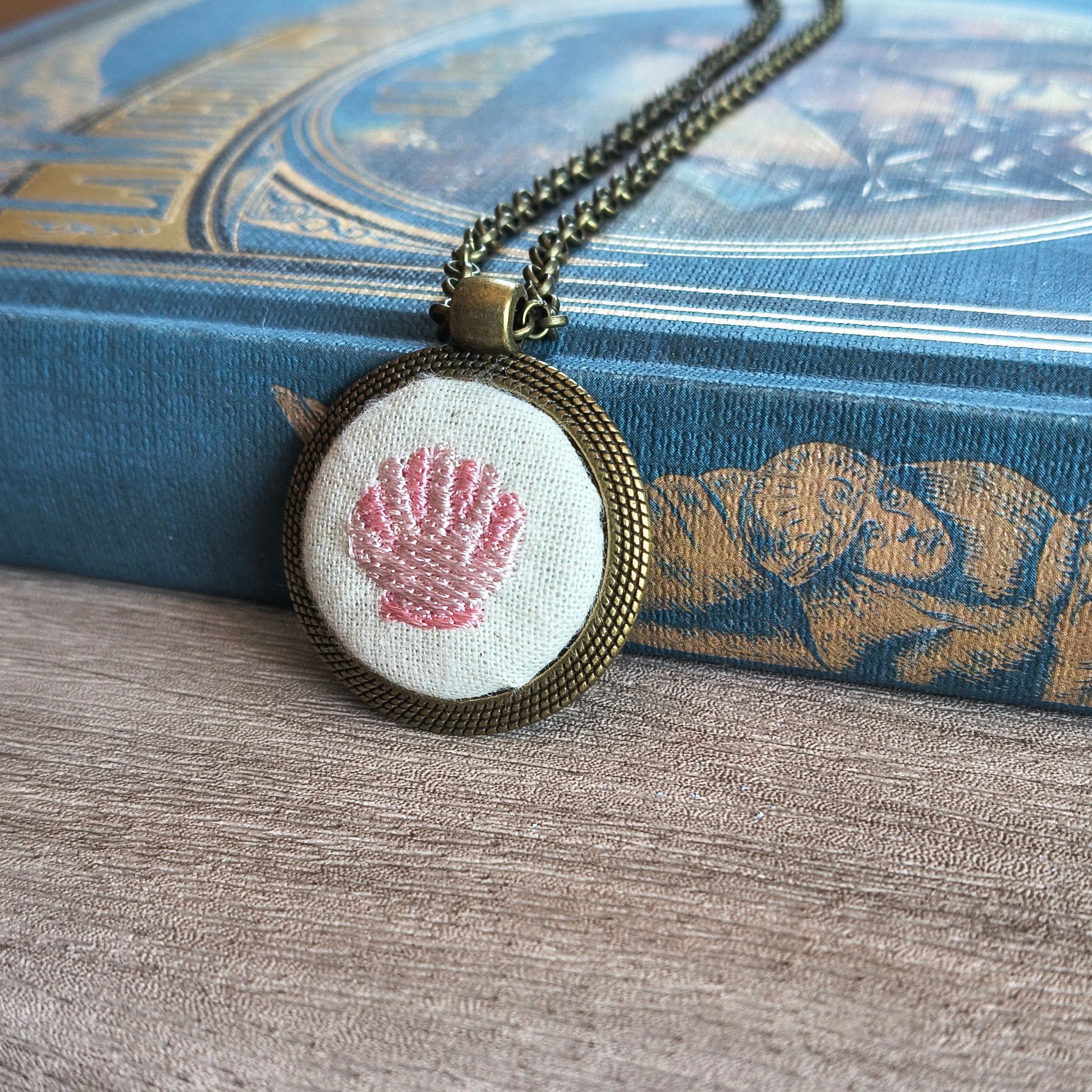 Collana artigianale con simbolo ricamato, realizzata a mano da Fildisogno, visibile in primo piano con dettagli tessili.