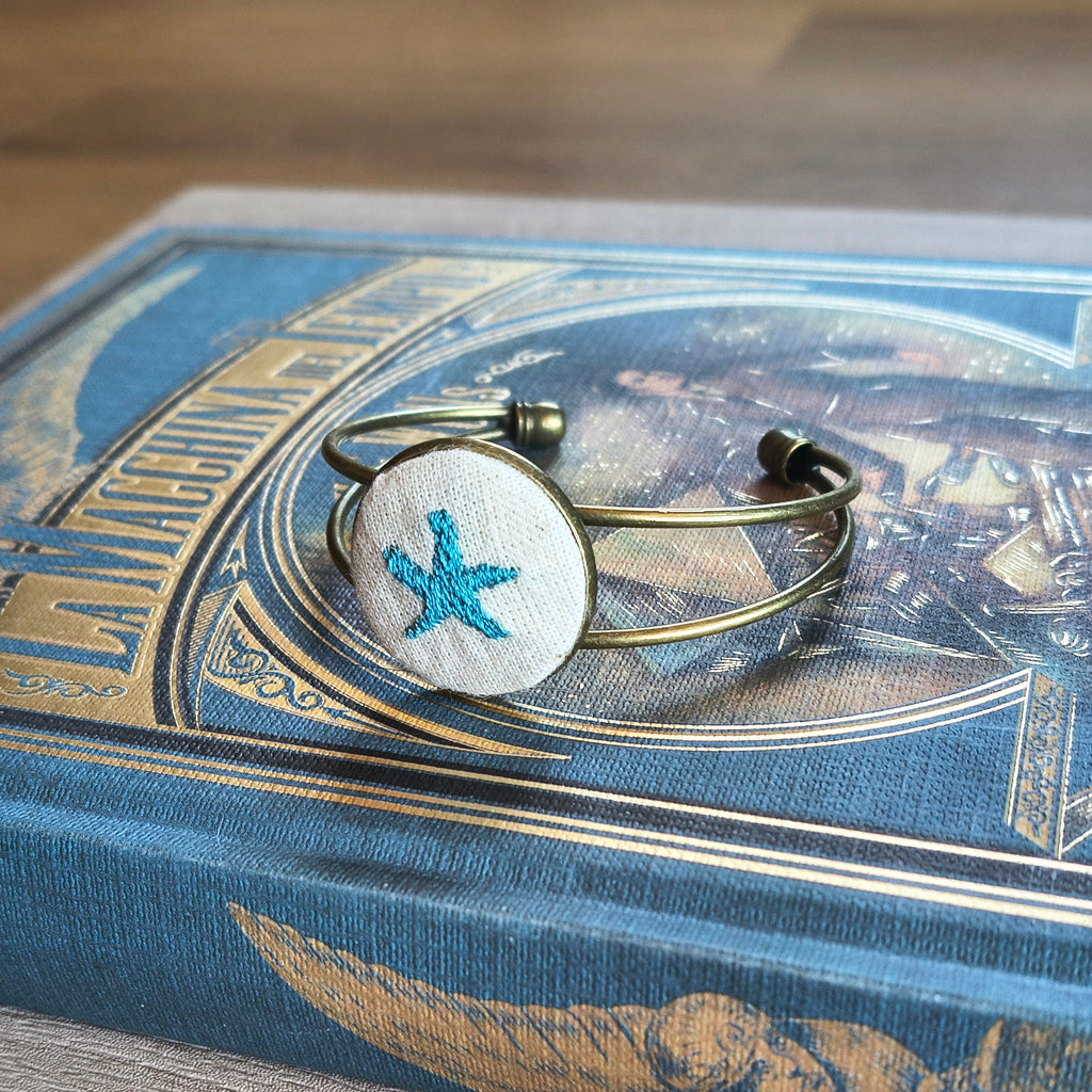 Bracciale artigianale Fildisogno con simbolo ricamato, dettagli intrecciati e finitura elegante, visibile in primo piano.