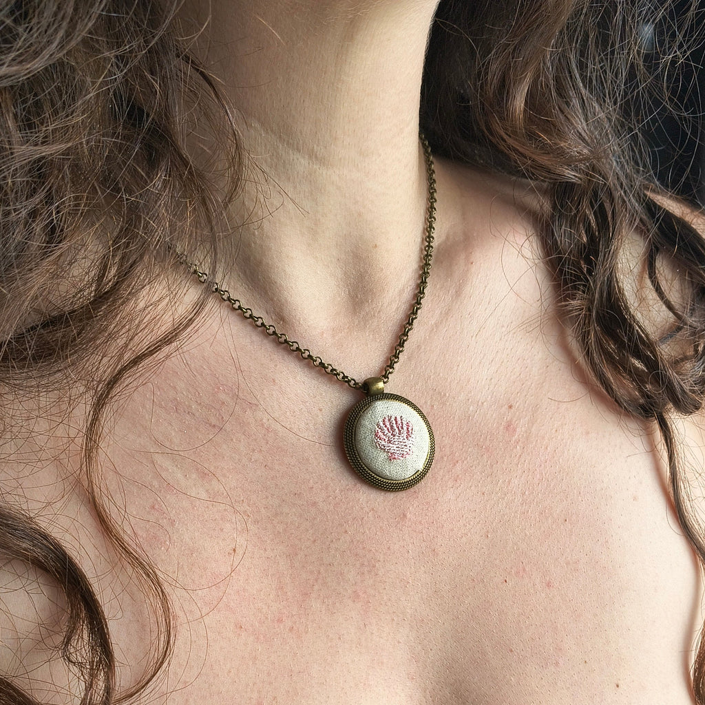 Collana artigianale con simbolo ricamato, elegante accessorio in tessuto, firma Fildisogno, indossata su sfondo neutro.