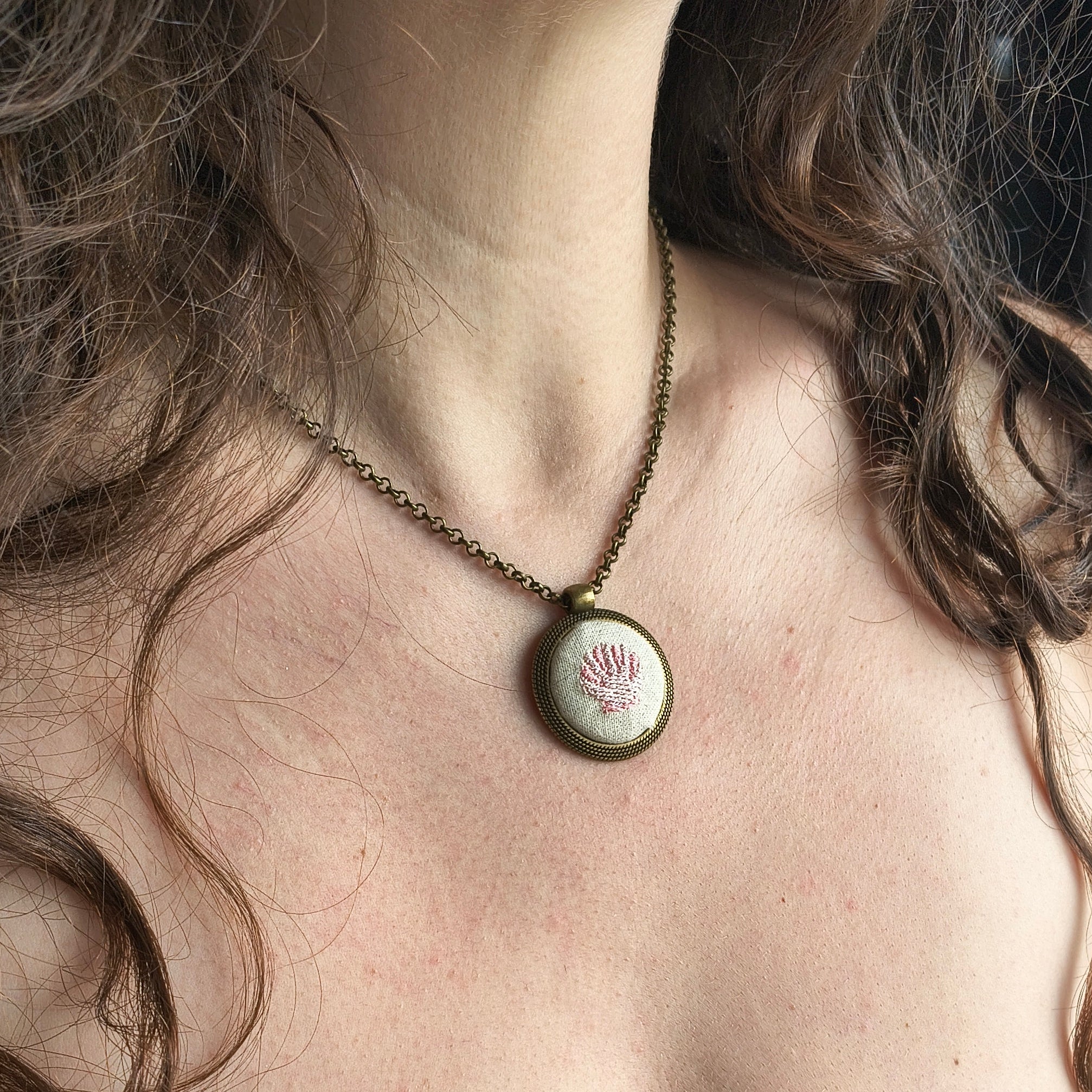 Collana artigianale con simbolo ricamato, elegante accessorio in tessuto, firma Fildisogno, indossata su sfondo neutro.