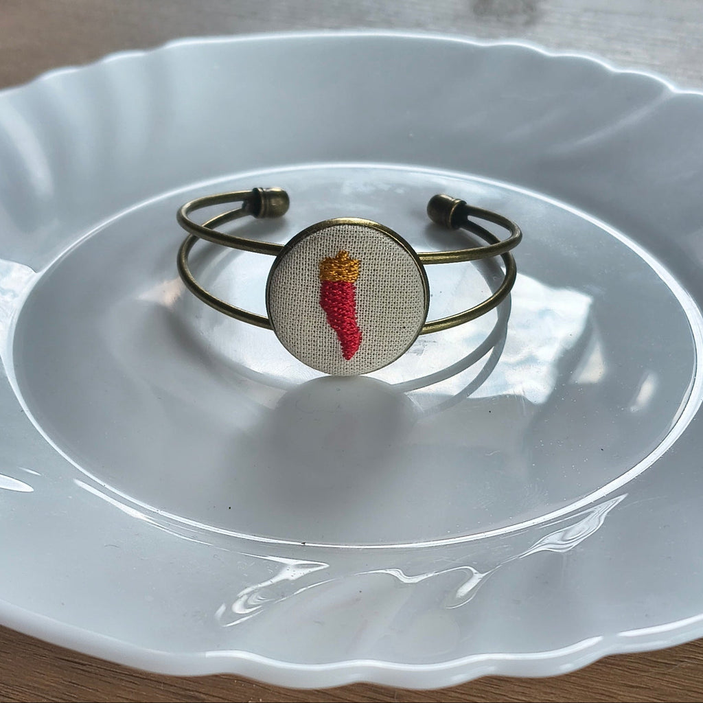 Bracciale artigianale Fildisogno con simbolo ricamato, dettagli in tessuto e finiture eleganti, visibile nell'immagine.
