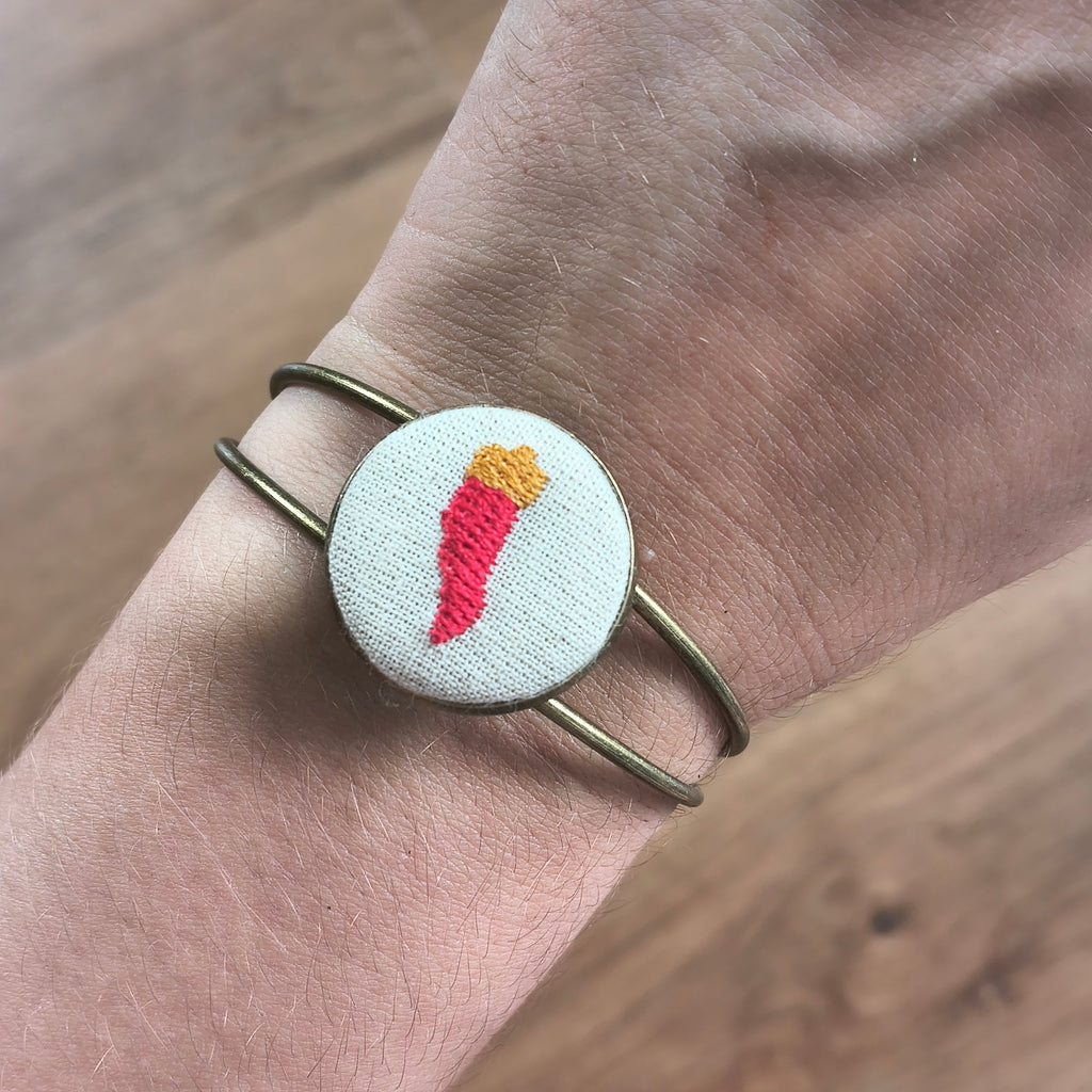 Bracciale artigianale Fildisogno con simbolo ricamato, dettaglio elegante e fatto a mano, visibile in primo piano nell'immagine.