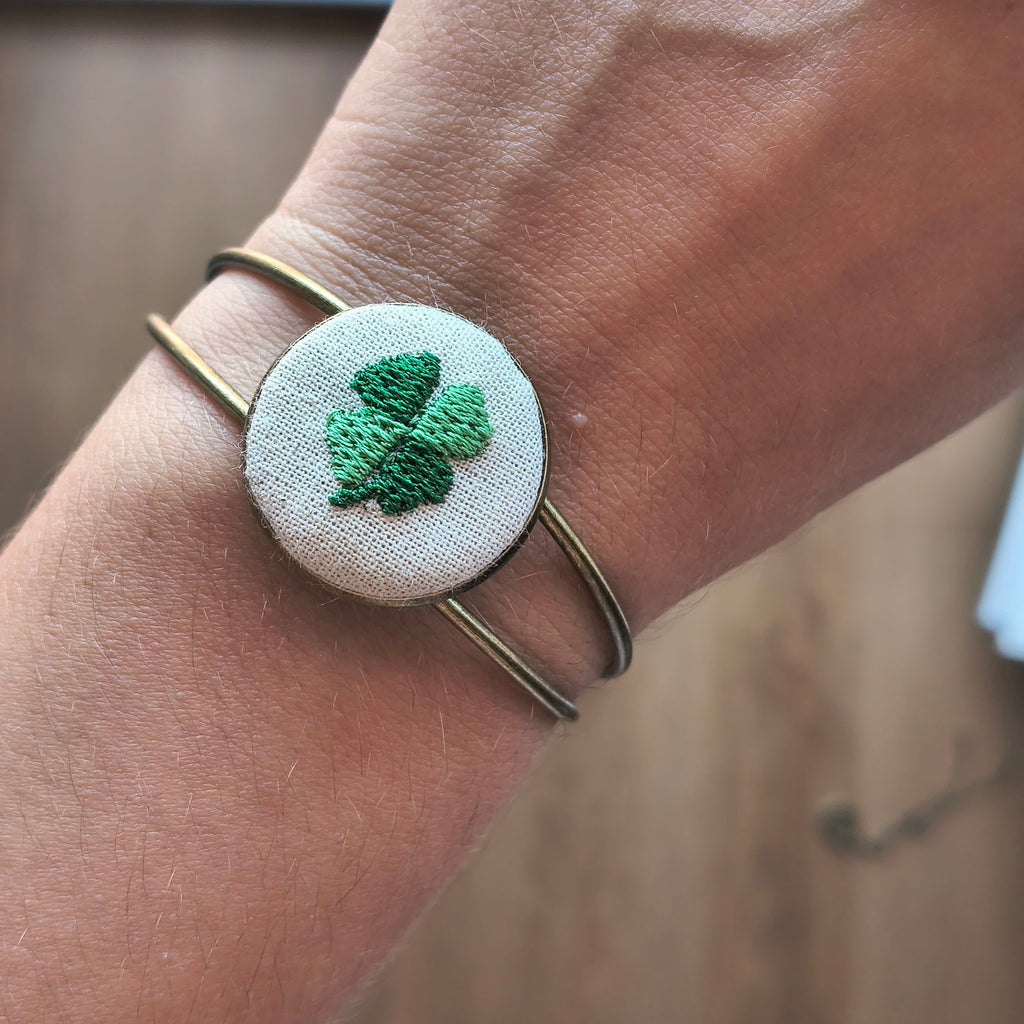 Bracciale artigianale Fildisogno con simbolo ricamato in tessuto colorato e dettagli eleganti, su sfondo neutro.